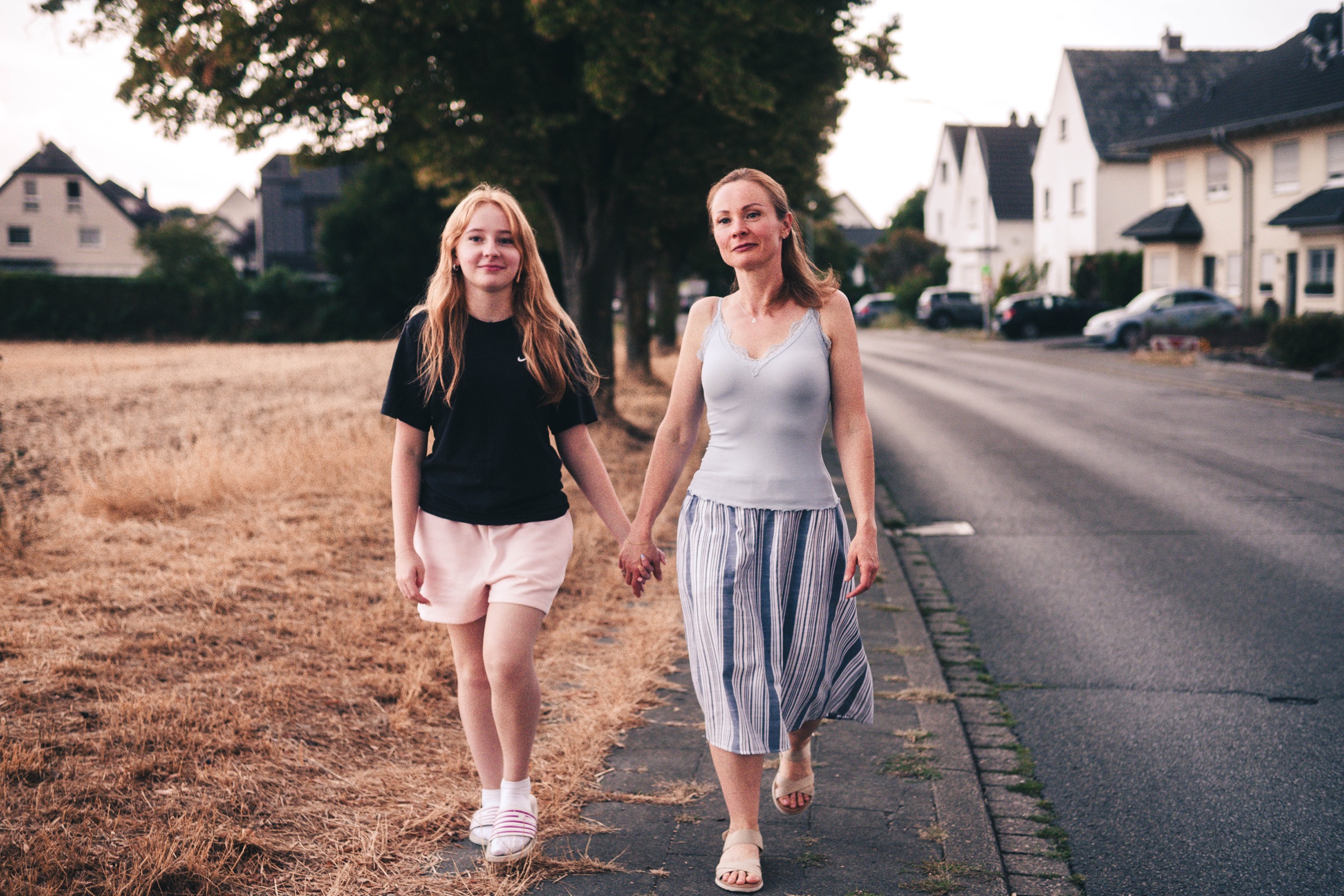 Mutter und Tochter gehen Hand in Hand am Abend durch ihre Nachbarschaft